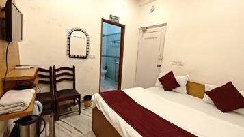 Habitación de hotel con una cama, una silla, un escritorio con computadora, un espejo y una puerta que da a un baño.