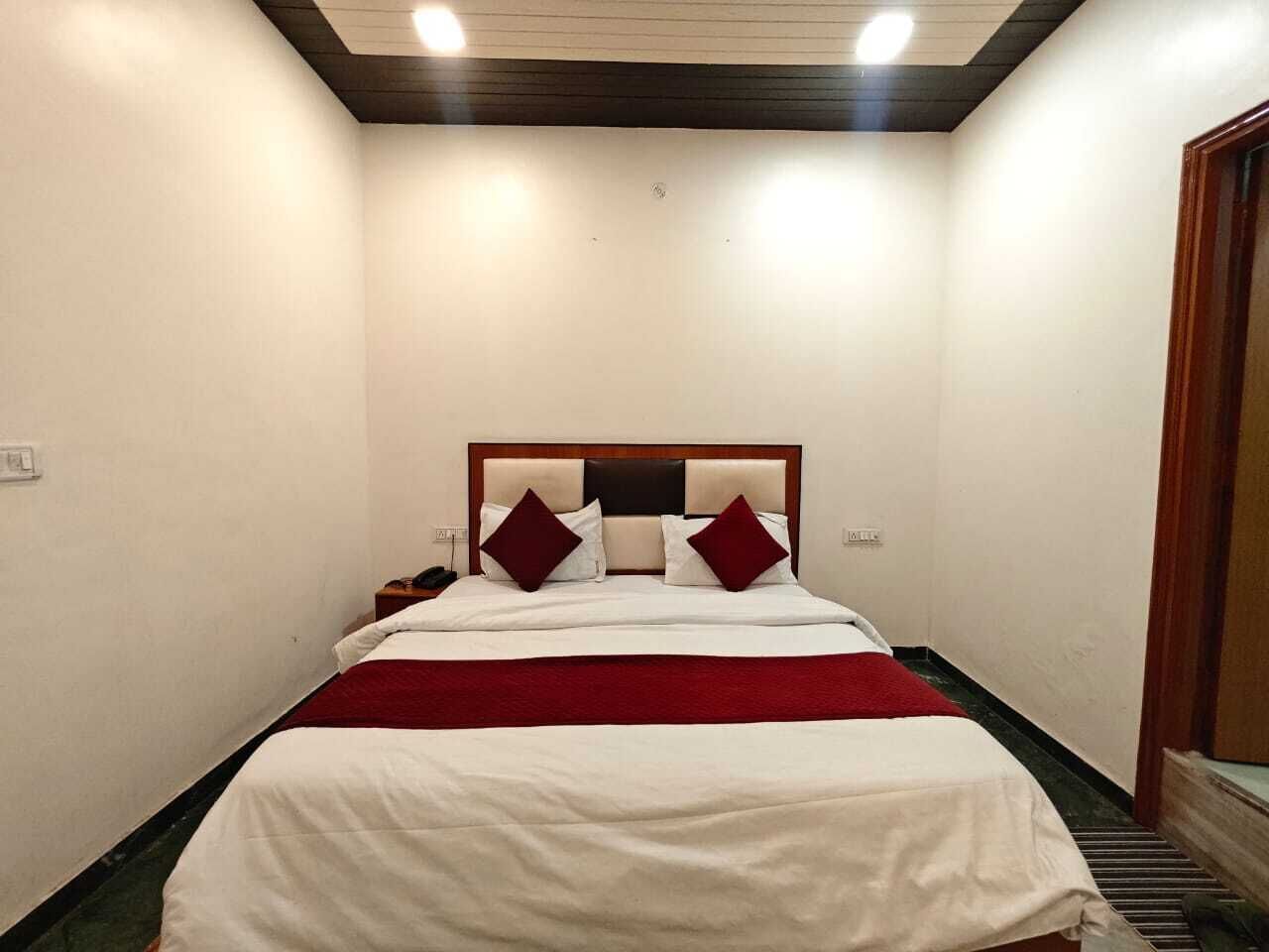 Quarto de hotel com uma cama, mesa de cabeceira e porta de madeira.