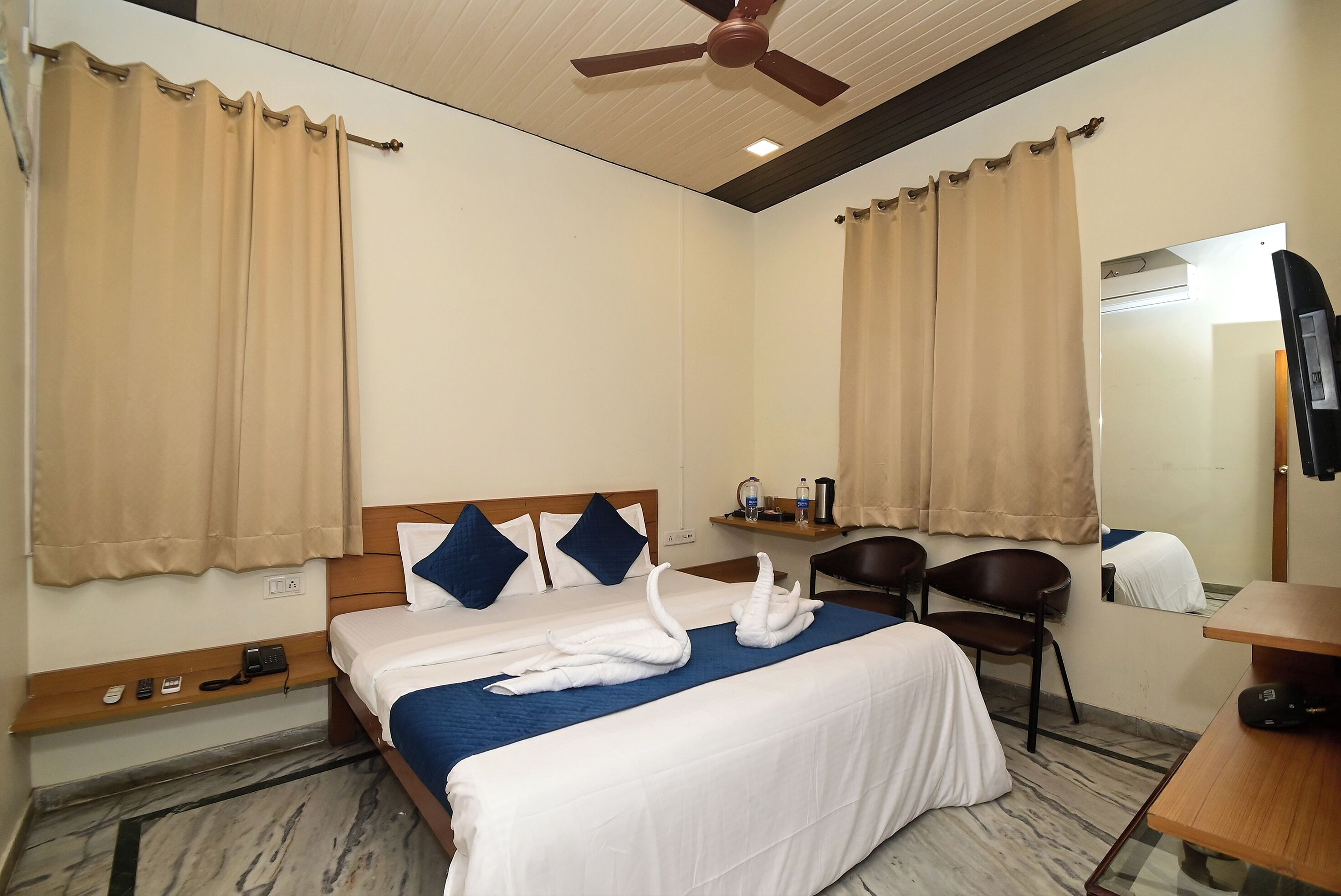 Una habitación de hotel con cama, escritorio, silla, ventilador de techo y espejo.