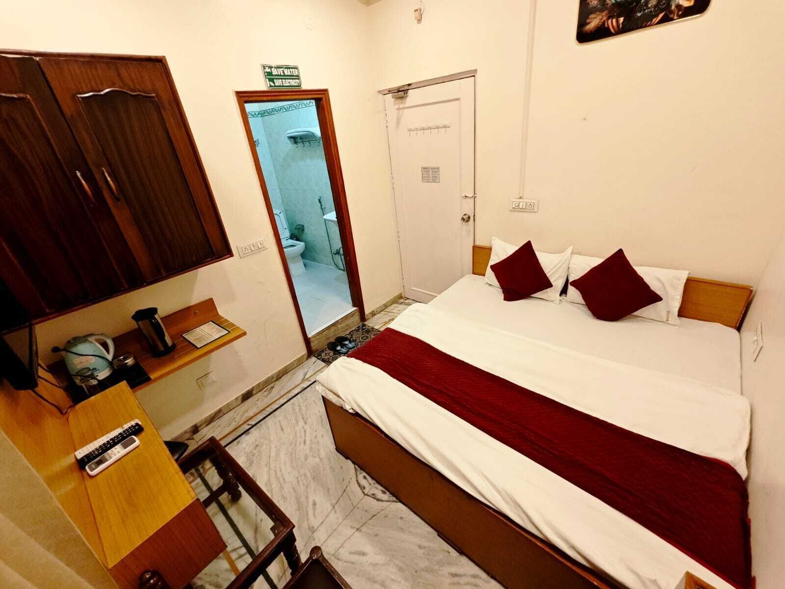 A hotel room with a bed, a wardrobe, a desk with a kettle, a mirror, and a door leading to a bathroom.