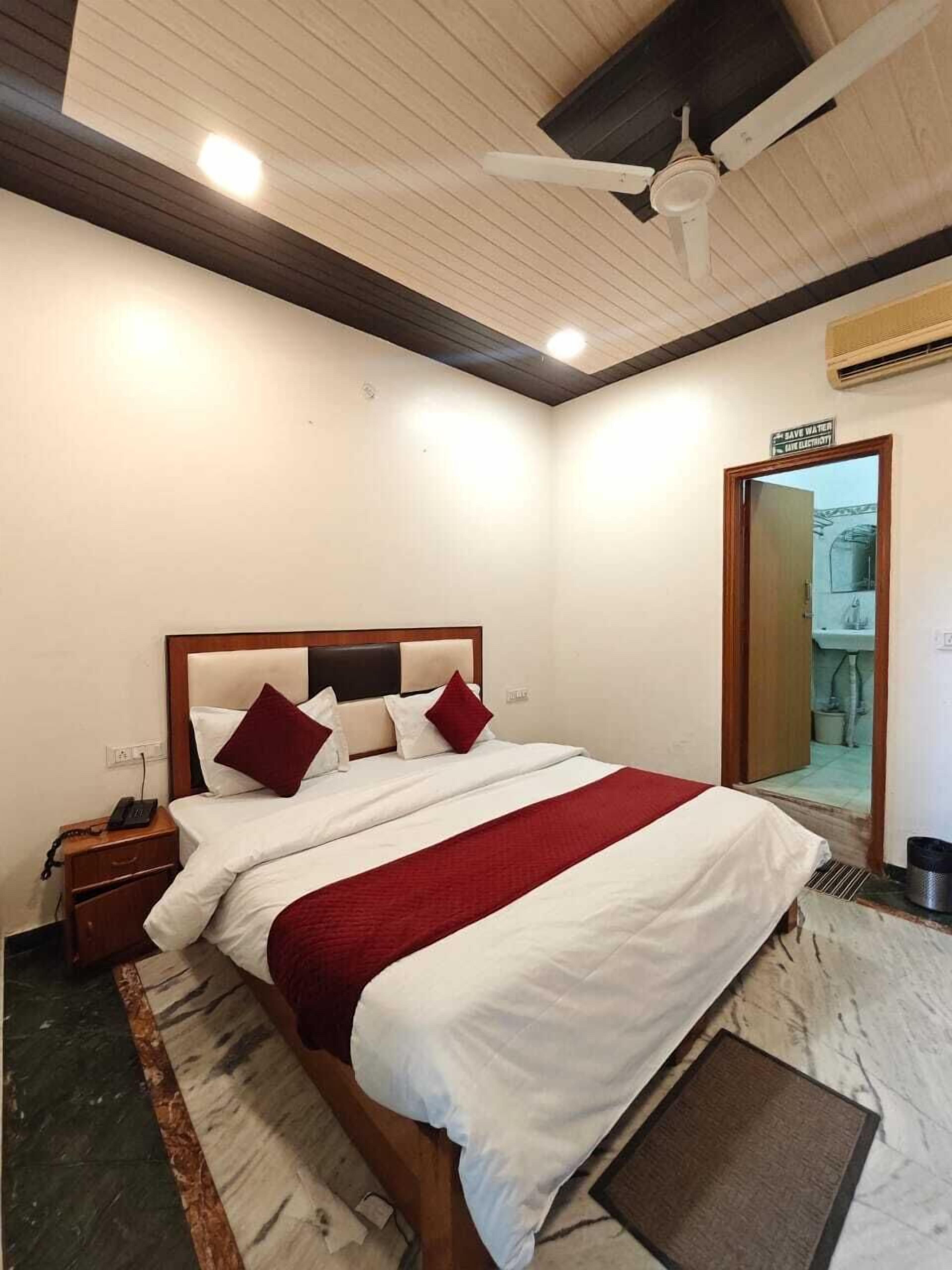 A hotel room with a bed, a nightstand, a ceiling fan, and a bathroom door.