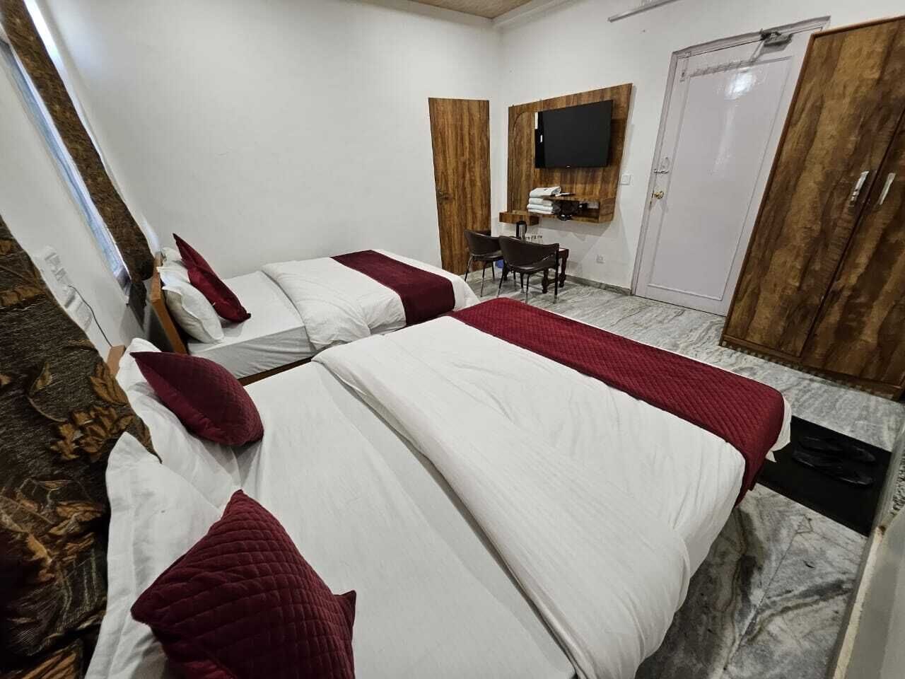 A hotel room with two beds, a TV mounted on the wall, and a wooden wardrobe.