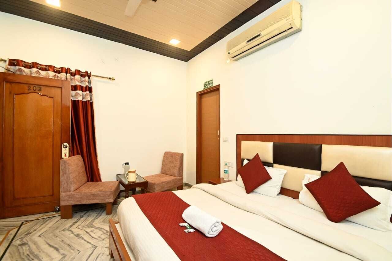 A hotel room with a bed, a chair, a desk, an air conditioner, and a door.