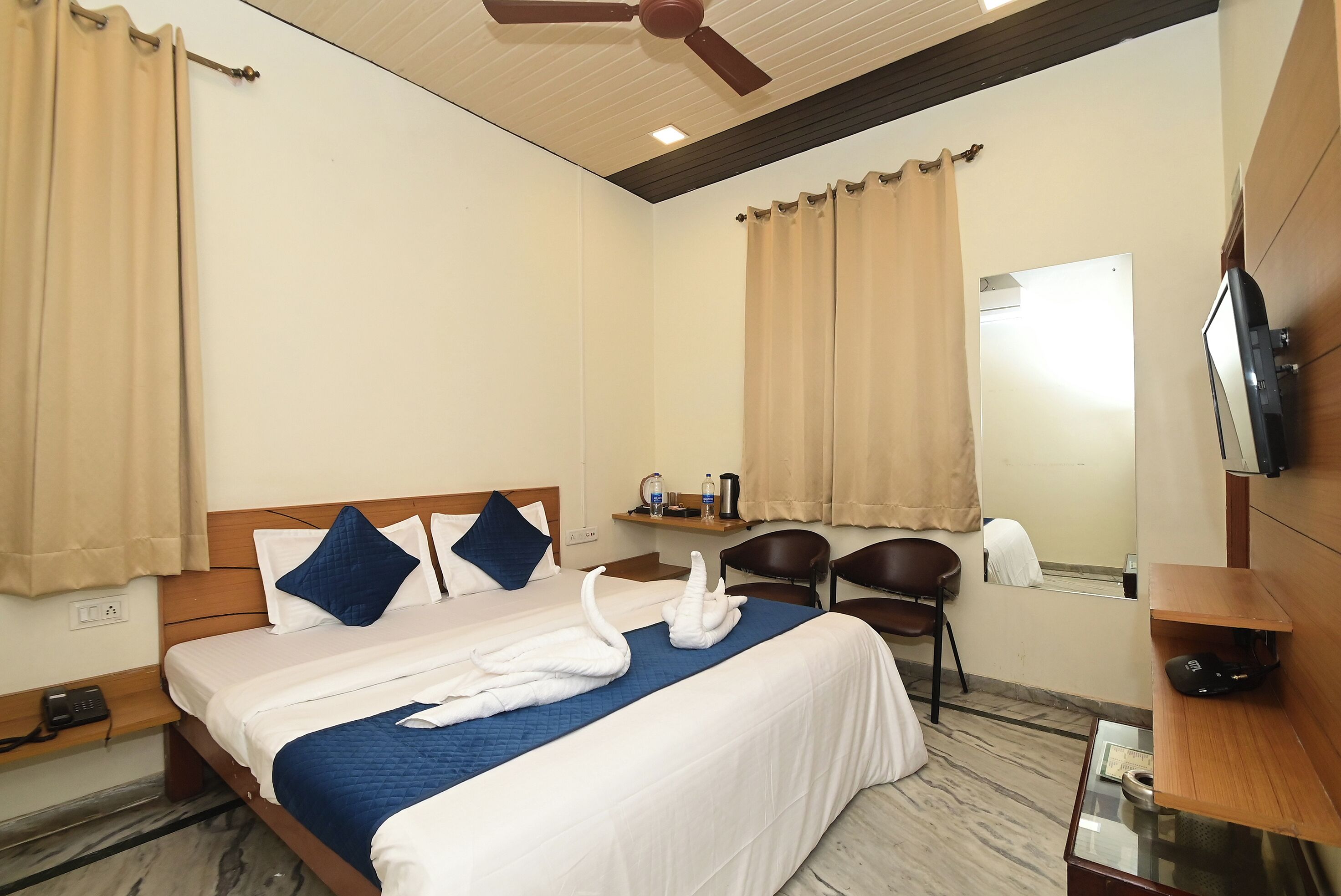 A hotel room with a bed, a desk, a chair, a television, and a ceiling fan.