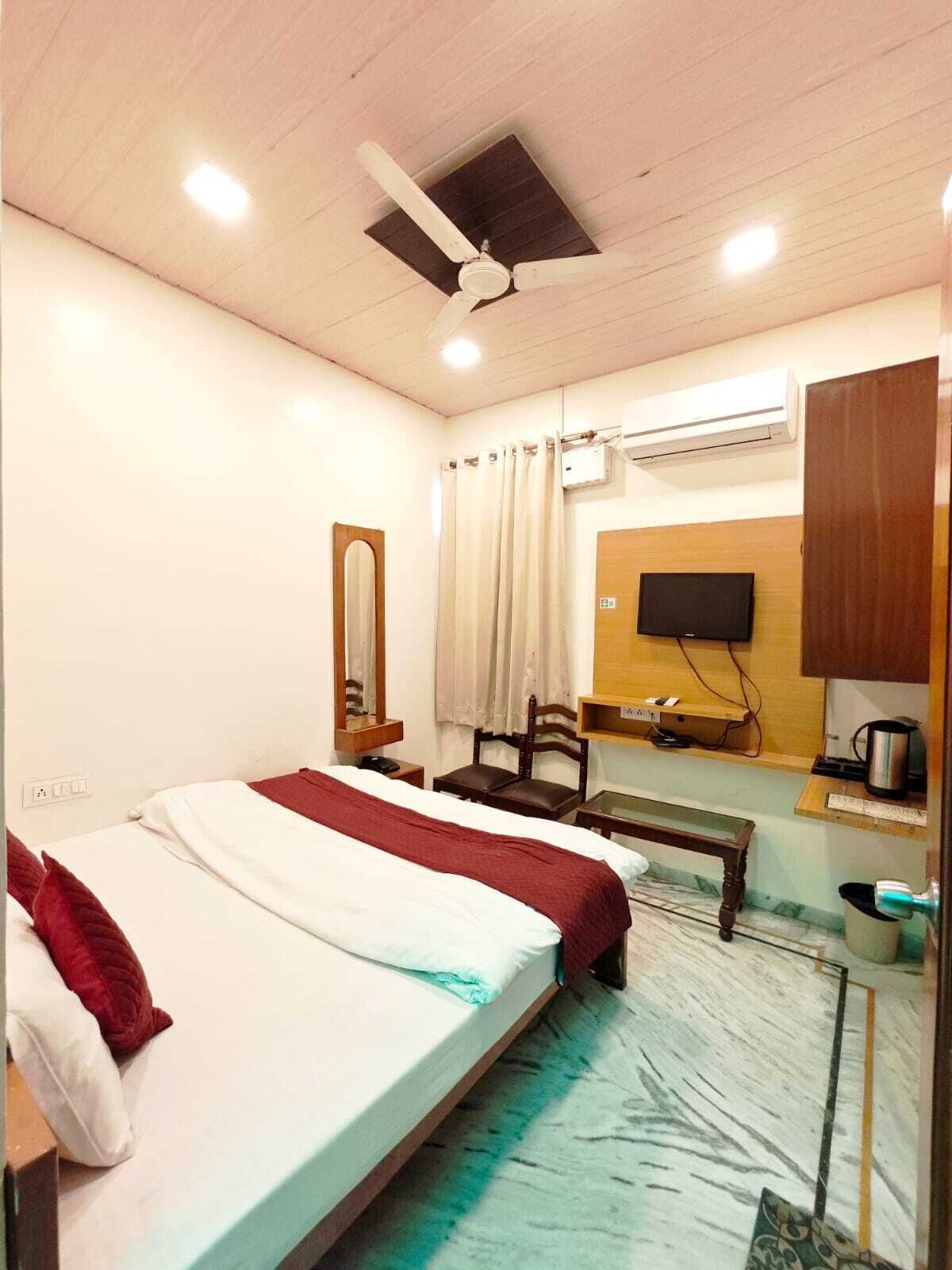 A hotel room with a bed, a desk, a chair, a television, and an air conditioning unit.