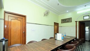 Una sala de conferencias con una larga mesa, sillas marrones, una pizarra y un refrigerador.