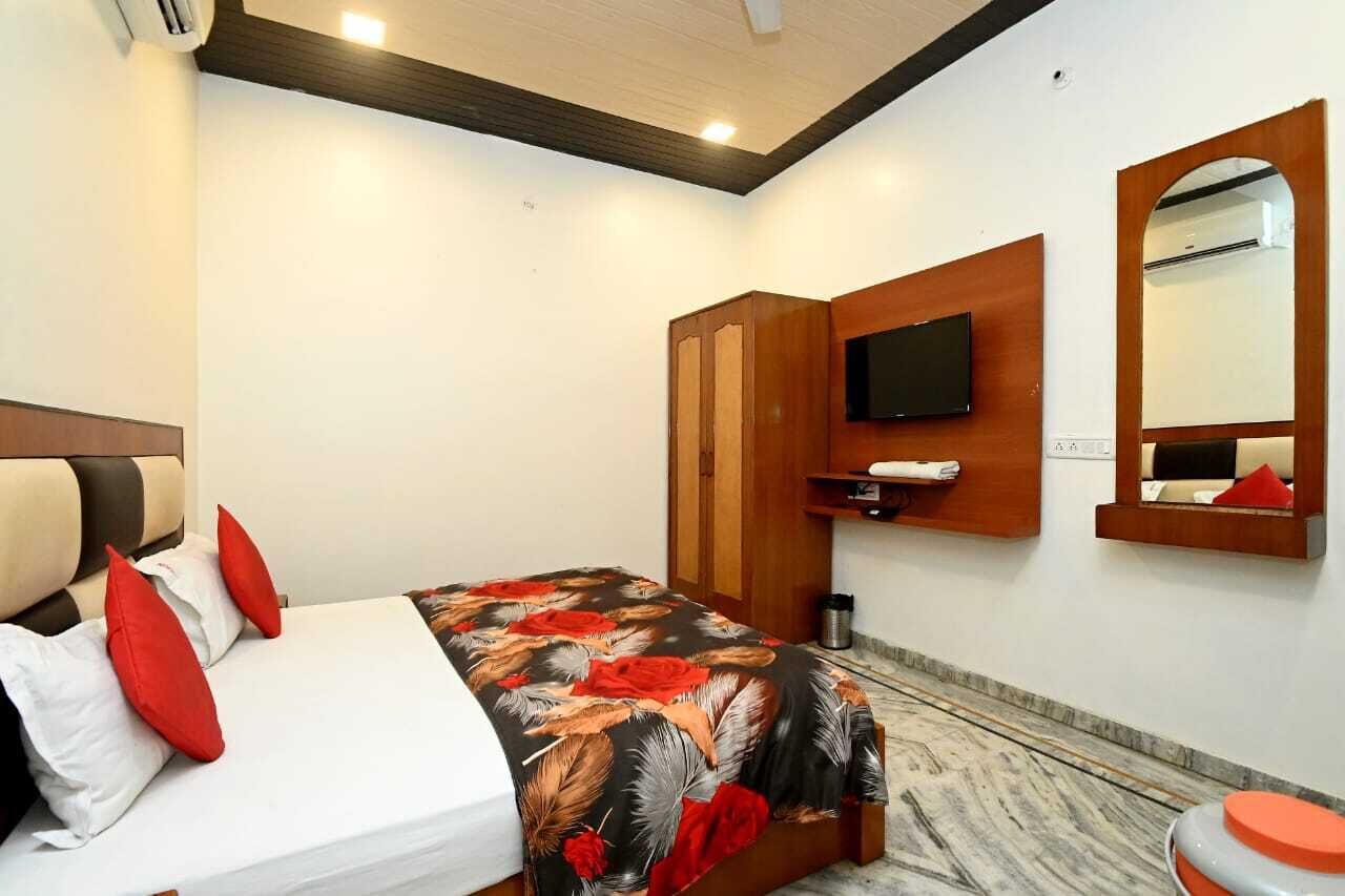 A hotel room with a bed, a TV, a mirror, and a small shelf.