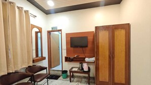 Una habitación con un armario de madera, un televisor montado en la pared, una mesita con una tetera y un par de sillas.