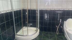 A bathroom with a glass-enclosed shower, a toilet, and black and white tiled walls. - UNIQUE GUEST HOUSE (Addis Ababa)