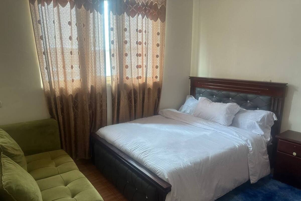 A bedroom with a bed, a green armchair, a wooden nightstand, and a blue rug.