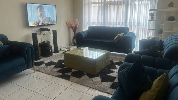 A living room with a TV, sofas, a coffee table, and a bookshelf. - UNIQUE GUEST HOUSE (Addis Ababa)