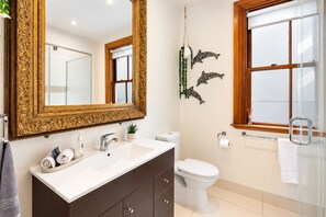 A bathroom with a large ornate mirror, a white sink, a toilet, and a window with a wooden frame.