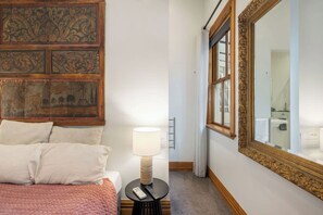 Quarto de hotel com cama, abajur, espelho e parede com painel decorativo.