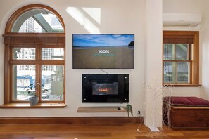A modern living room with a fireplace, a television mounted on the wall, and large windows offering a view of the cityscape.