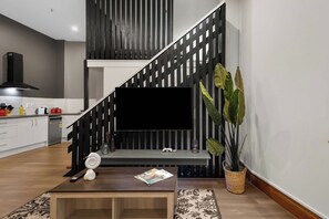 A modern living room with a staircase, a flat-screen TV, a coffee table, and a potted plant. - Lambton Quay Loft - Sleeps 10 (Wellington)