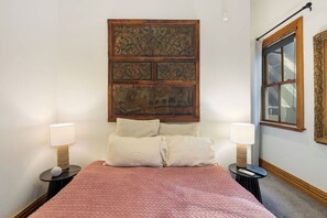 A bedroom with a large wooden headboard, two bedside tables with lamps, a pink quilted bedspread, and a window with a view. - Lambton Quay Loft - Sleeps 10 (Wellington)