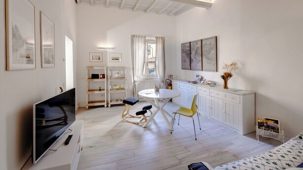 A modern living room with a flat-screen TV, a dining table with chairs, a kitchen area, and a bookshelf. - Bright Apartment a few steps from Duomo and Train Station. Wifi, A/C, W&D  (Firenze)