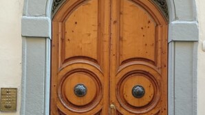 A double wooden door with a decorative arch and two round metal handles. - Bright Apartment a few steps from Duomo and Train Station. Wifi, A/C, W&D  (Firenze)
