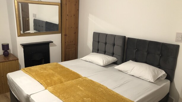 Ein Schlafzimmer mit einem Bett, einem Spiegel, einem Holzschrank und einem kleinen Tisch mit einer Lampe.
