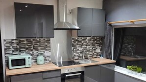 Moderni keittiö, jossa on tummat kaapit, ruostumattomasta teräksestä valmistettu liesituuletin, mikroaaltouuni ja sisäänrakennettu uuni.