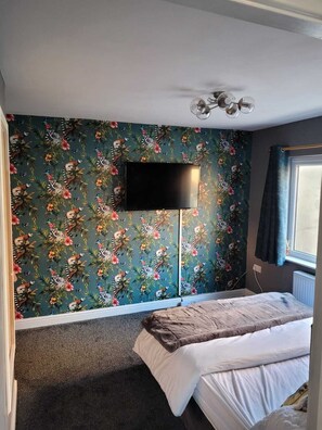 A bedroom with a bed, a flat-screen TV mounted on the wall, and a window with curtains. - Family Holiday Apartment Blackpool South Shore (Blackpool)