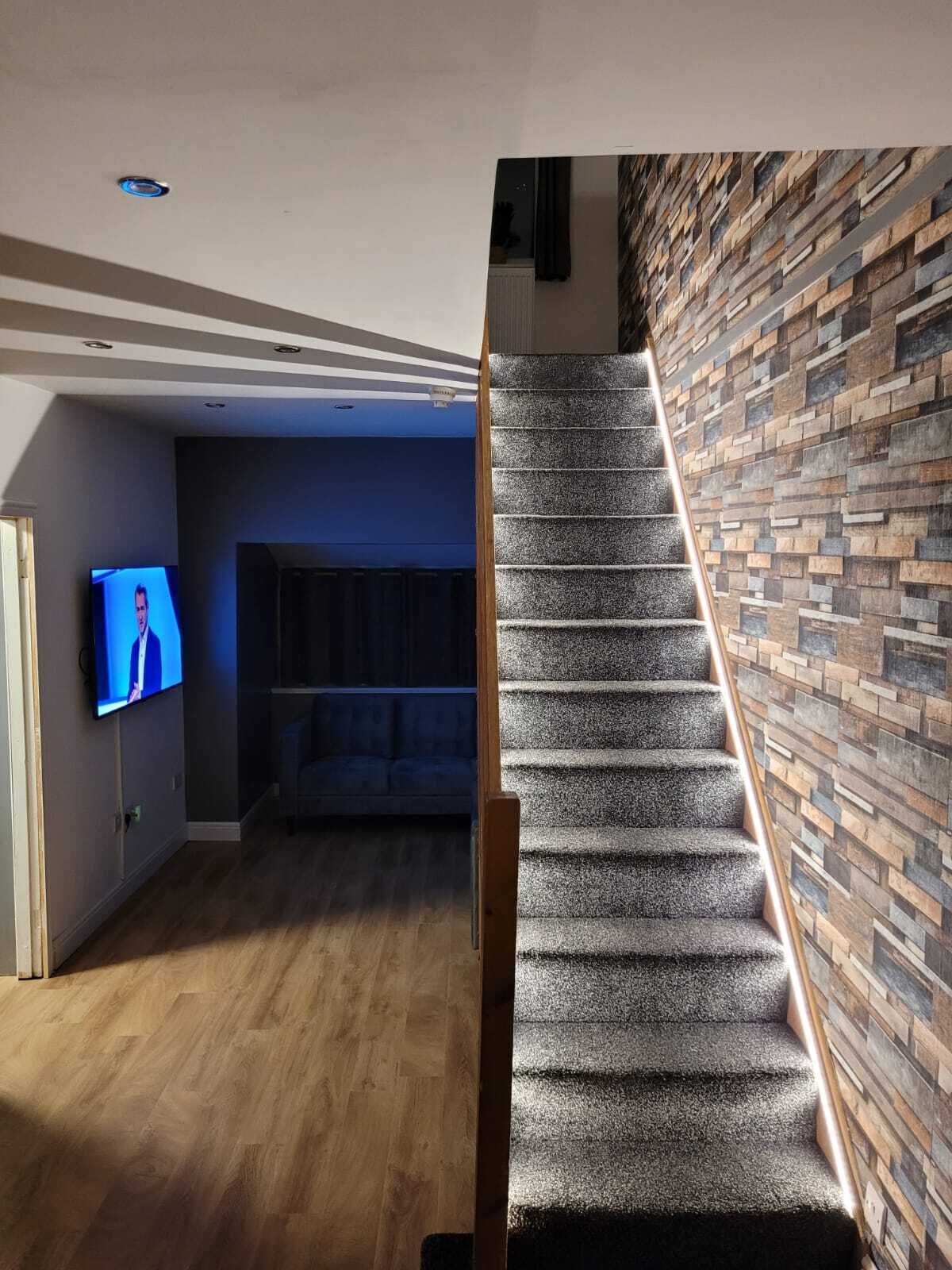 A staircase with a wooden handrail leading to a living area with a TV, a sofa, and a patterned wall.