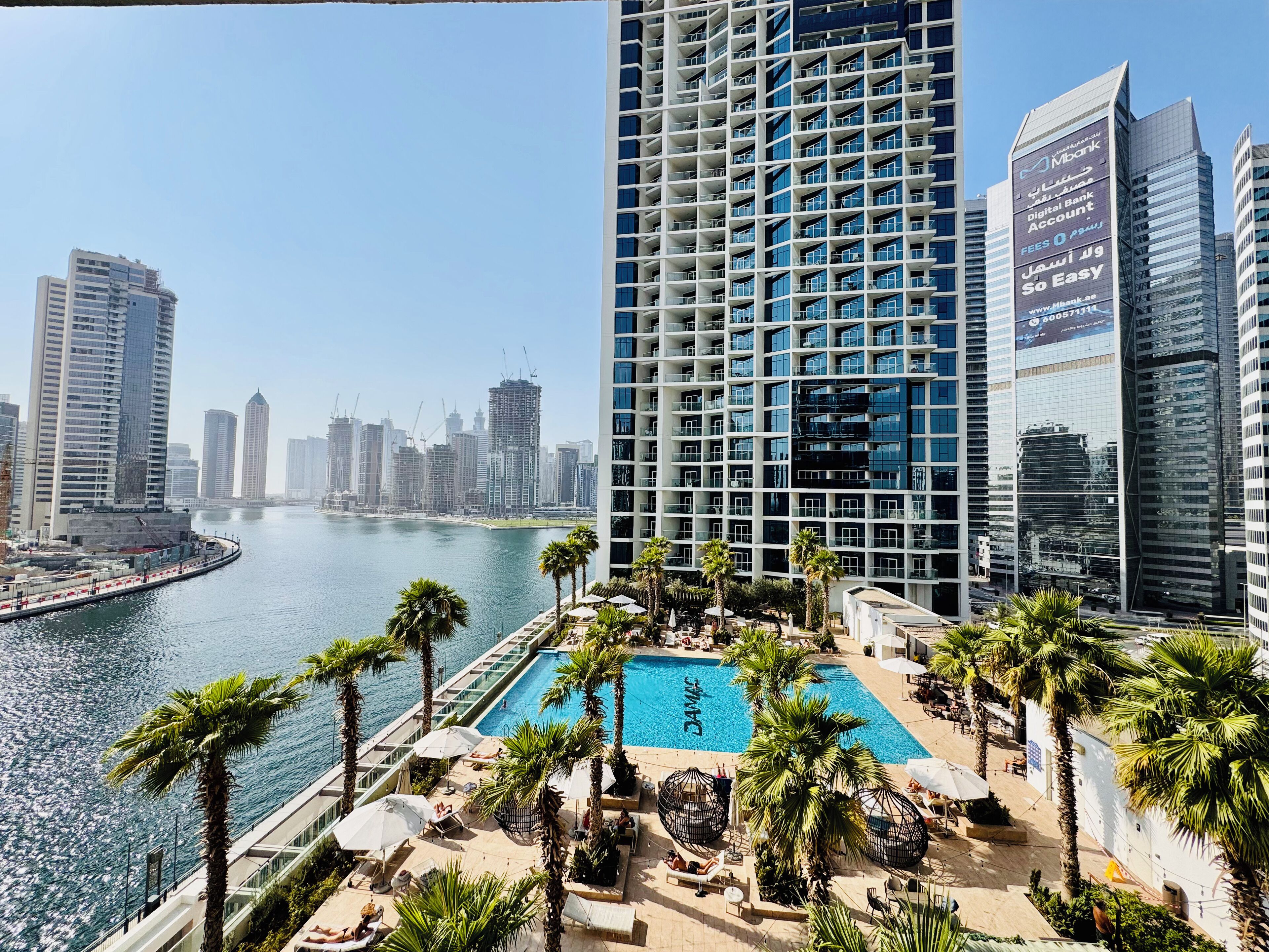 A high-rise hotel with a pool area, palm trees, and a view of the city skyline.