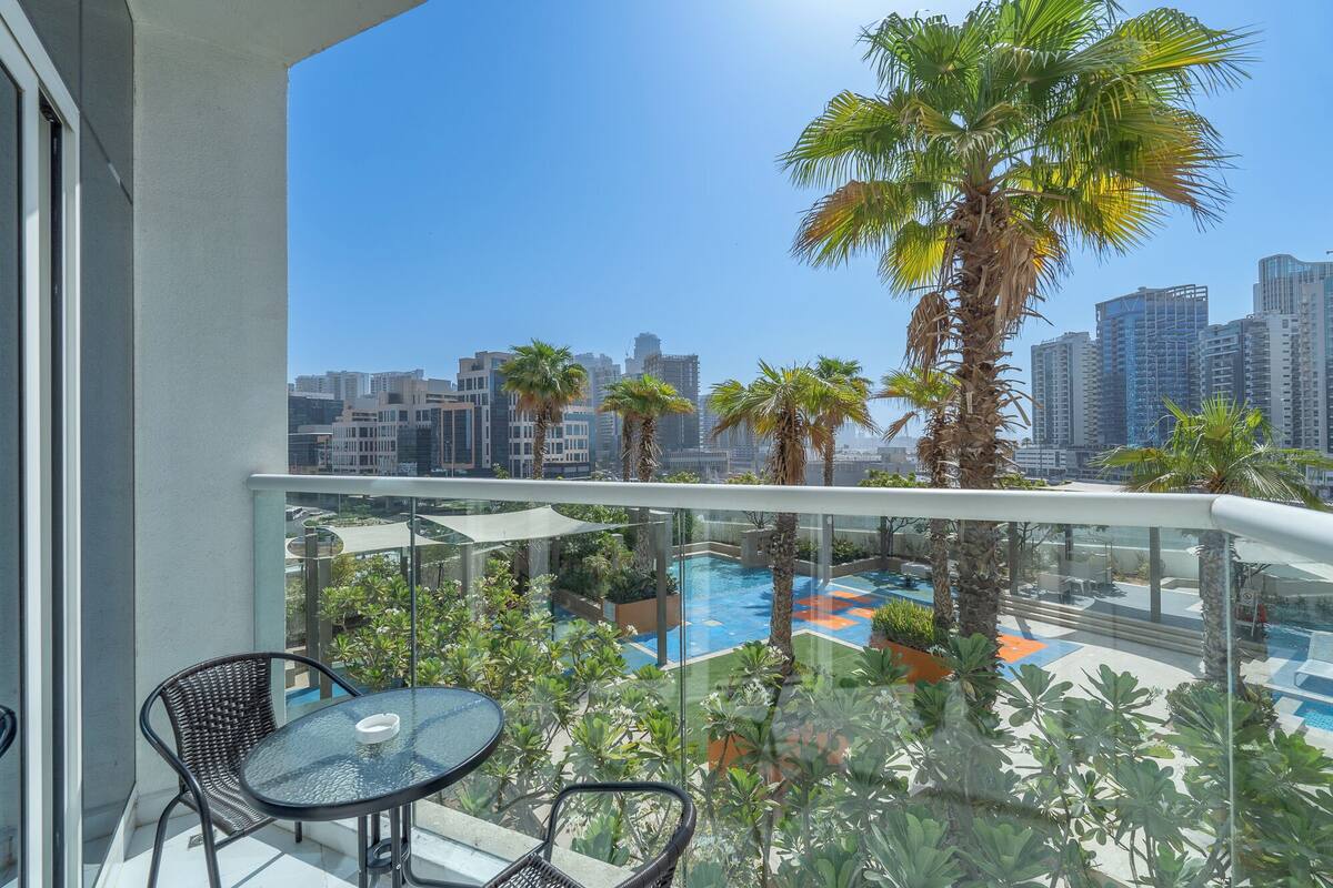 A balcony with a glass railing, a pool, and palm trees.