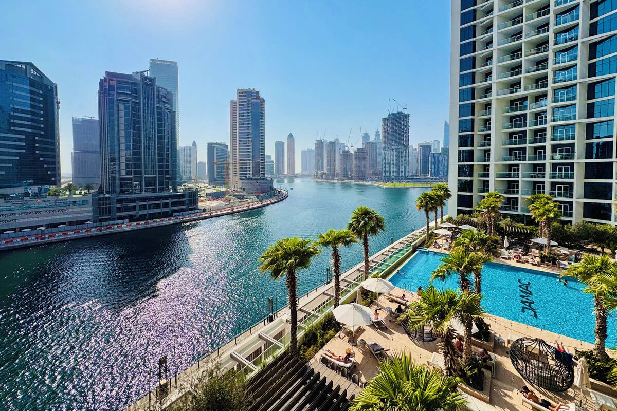 A high-rise hotel with a pool area, overlooking a body of water with a cityscape in the background.