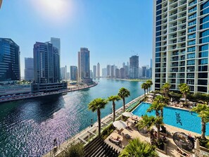 A high-rise hotel with a pool area, overlooking a body of water with a cityscape in the background.