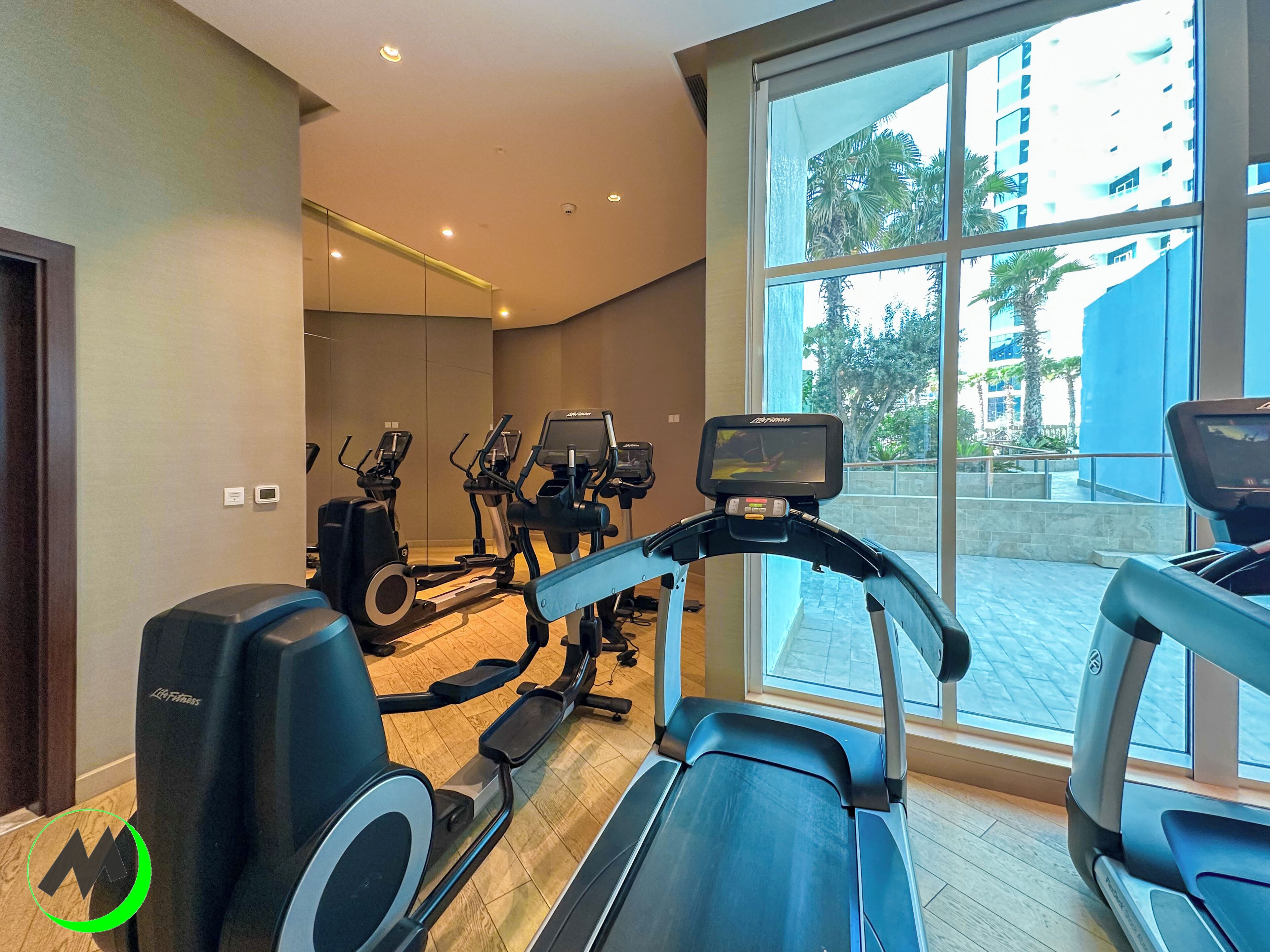 A gym with treadmills, ellipticals, and a large window offering a view of the outside.