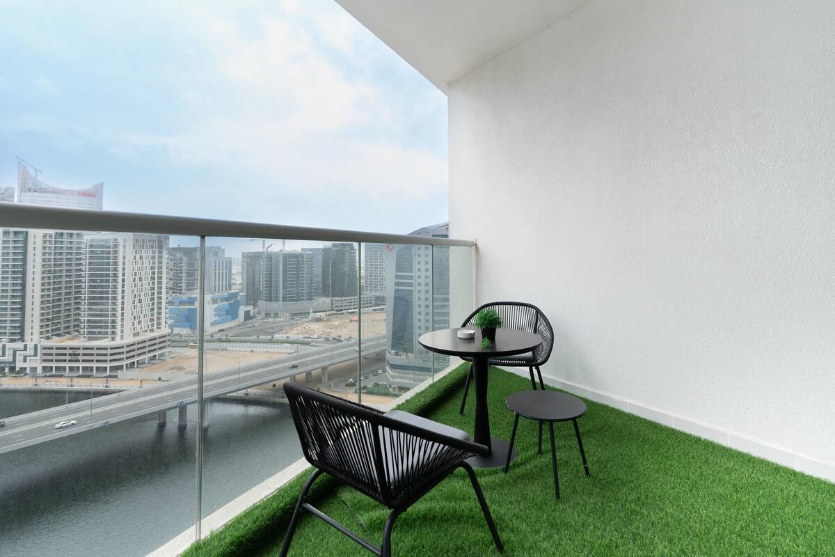 A balcony with a view of a cityscape, a small table with a plant, and two chairs.