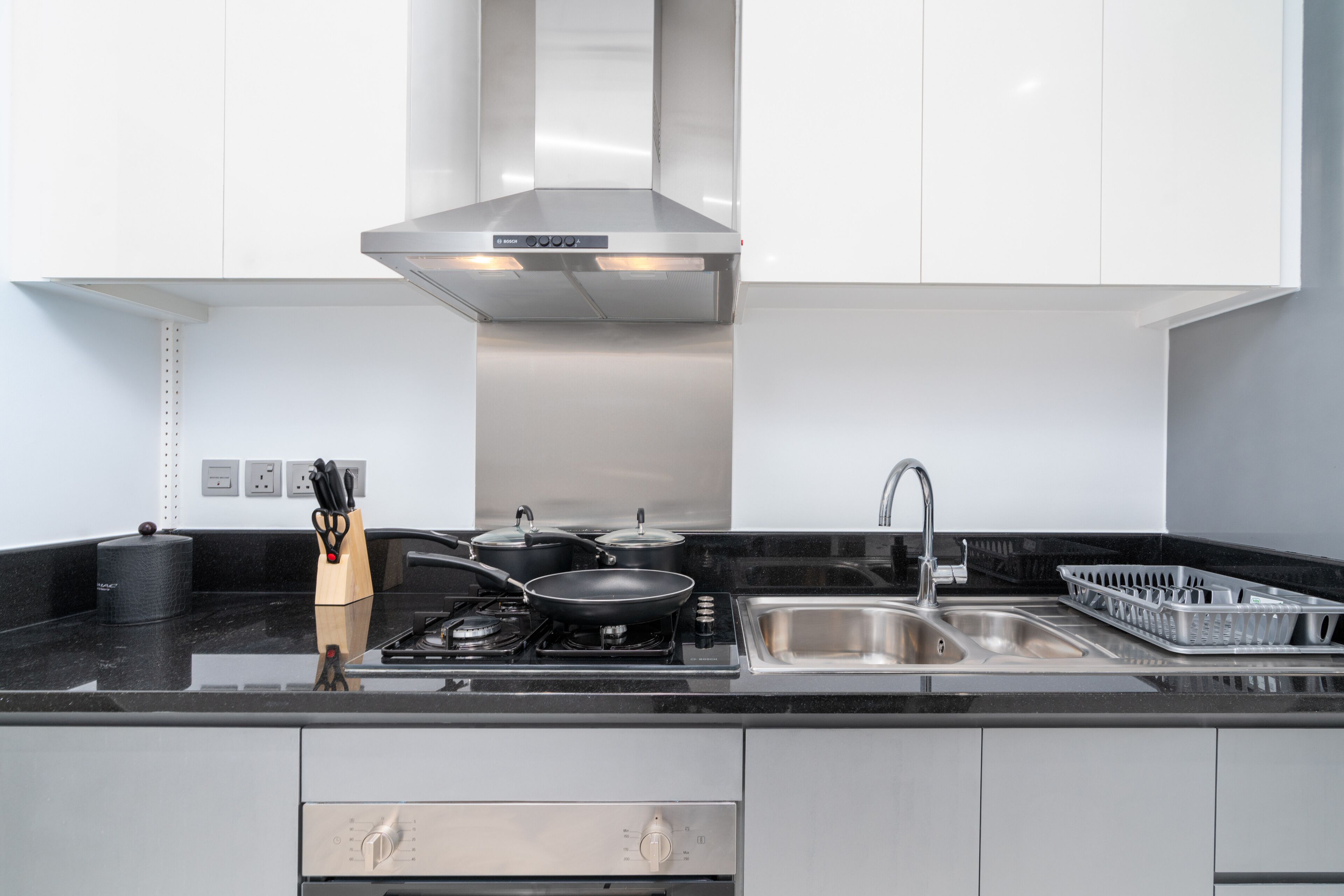 Une cuisine moderne dotée d’appareils électroménagers en acier inoxydable, d’un plan de travail noir et de meubles blancs.