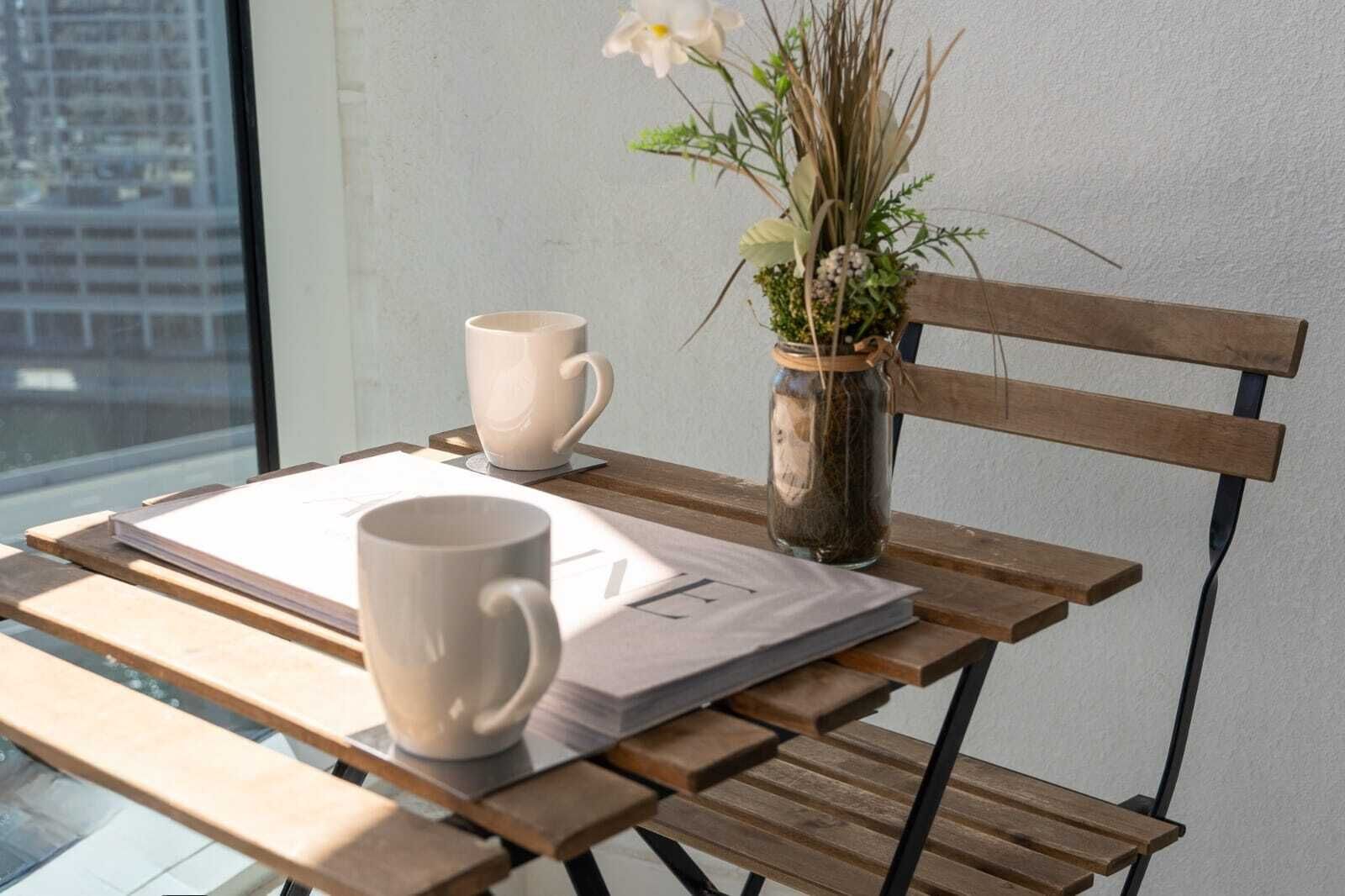 A wooden table with two white mugs and a small vase with dried plants.