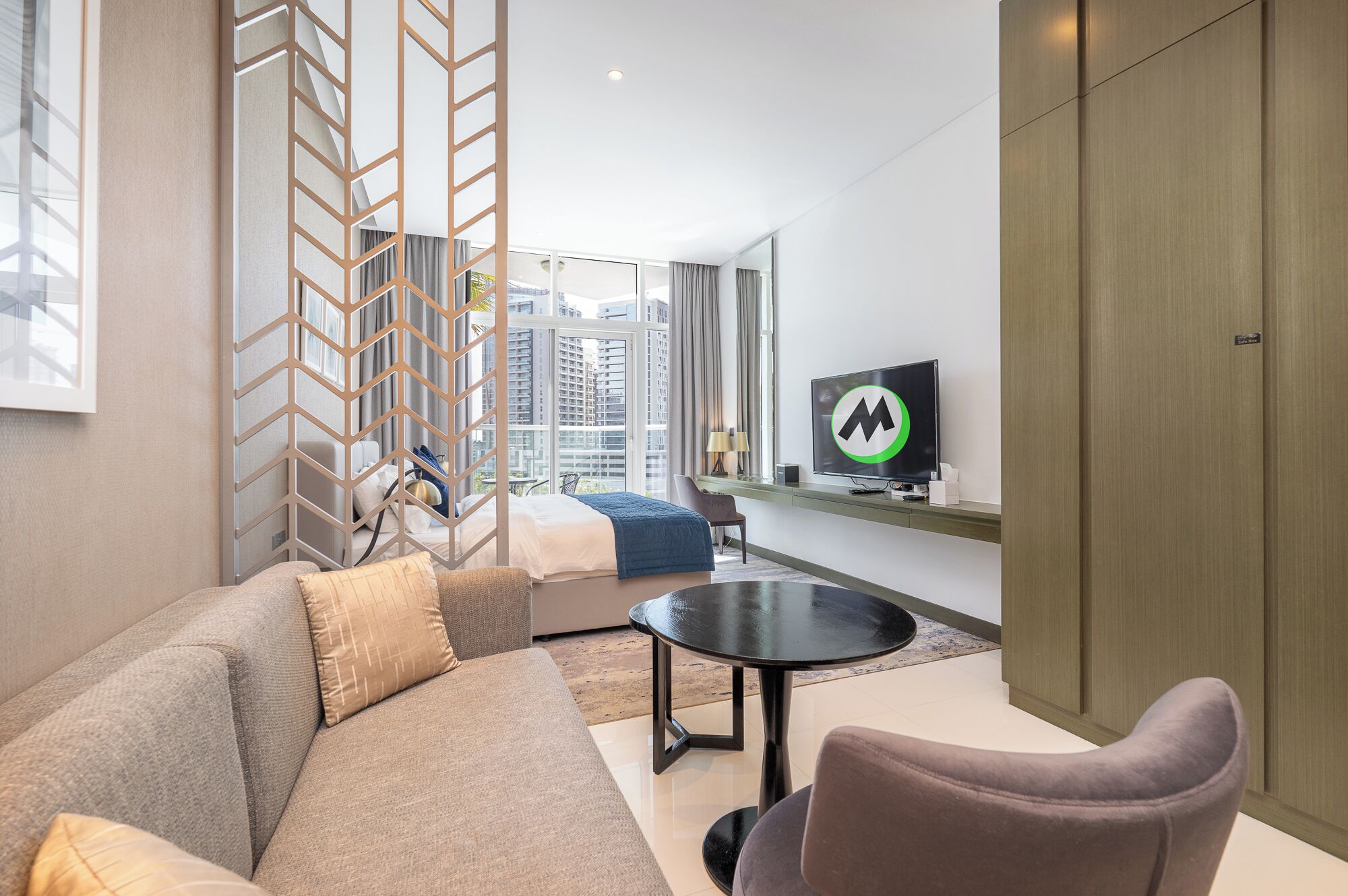 A modern hotel room with a sofa, a small table, a TV, and a view of the city.