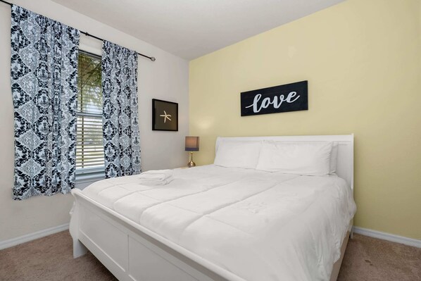 A bedroom with a white bed, a yellow wall, and a 'love' sign.