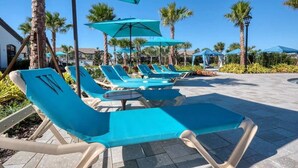 Een zwembadterras met ligbedden en parasols, palmbomen en een heldere lucht.
