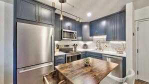 A modern kitchen with dark blue cabinets, stainless steel appliances, and a wooden dining table.