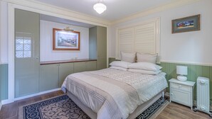 A bedroom with a bed, bedside table, nightstand, and a framed picture on the wall.