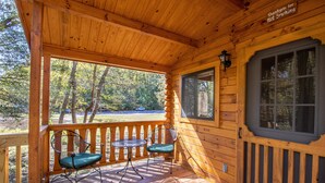A wooden cabin with a porch, two chairs, a table, and a window with a sign saying "Thank you for not smoking." - Lakeview Camp Cottage at Wilderness Presidential (Spotsylvania)