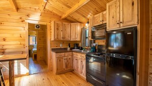 A wooden cabin interior with a kitchen area featuring wooden cabinets, a stainless steel refrigerator, and a stove. - Lakeview Camp Cottage at Wilderness Presidential (Spotsylvania)