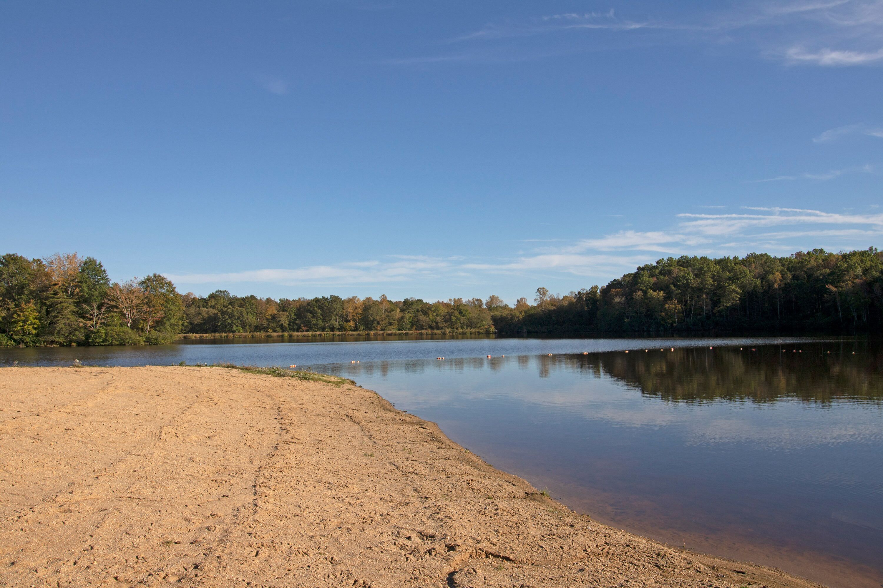 A sandy beach with a calm lake and forested hills in the background.
