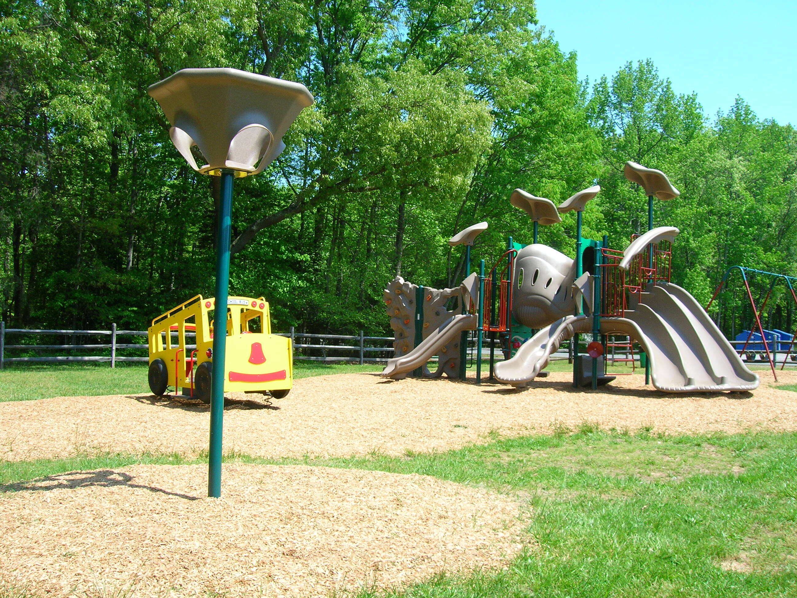A playground with a yellow vehicle, climbing structures, and slides.