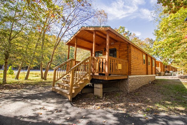 A wooden cabin with a porch and stairs, surrounded by trees and a clear sky.