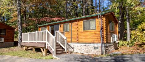 Step into this cozy cabin surrounded by a forest, featuring a front porch and a staircase leading to the entrance.