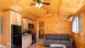 L’intérieur d’une cabane en bois comprend un coin cuisine, un canapé gris et un ventilateur de plafond.