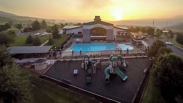 A swimming pool with slides and a playground, surrounded by buildings and a sunset.