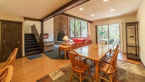 A spacious dining area with a large wooden table and chairs, a fireplace, and a view of the outdoors through large windows.