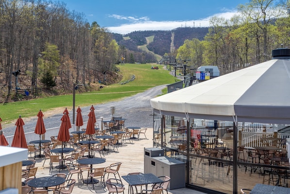An outdoor terrace with tables and chairs, overlooking a forested valley.