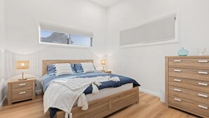 Quarto com cama de madeira, duas mesas de cabeceira, um criado-mudo e uma cômoda, além de janela com vista.